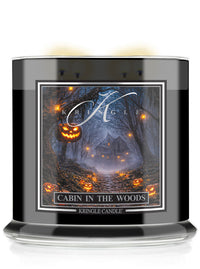 A Kringle Candle jar in a black glass container with a Halloween-themed label reading 'Cabin in the Woods.' The label shows a dark forest scene with glowing jack-o'-lanterns and a cabin, with the Kringle Candle brand name visible.