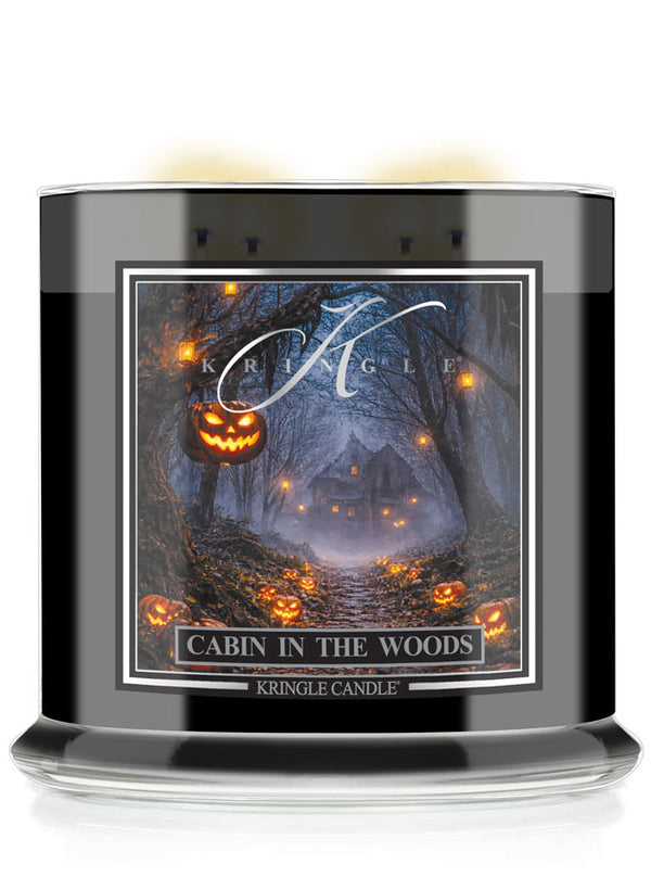 A Kringle Candle jar in a black glass container with a Halloween-themed label reading 'Cabin in the Woods.' The label shows a dark forest scene with glowing jack-o'-lanterns and a cabin, with the Kringle Candle brand name visible.