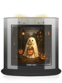 A large scented candle in a clear glass jar with a black base, featuring a Halloween-themed printed label. The label shows a ghost alligator holding a glowing jack-o'-lantern in a spooky forest scene with pumpkins and houses.