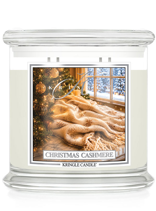 A Kringle Candle jar candle labeled 'Christmas Cashmere' with cream-colored wax in a clear glass container, featuring a festive label showing a cozy winter scene with a tree, blanket, and snowy window.