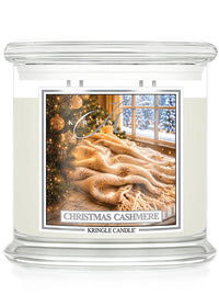 A Kringle Candle jar candle labeled 'Christmas Cashmere' with cream-colored wax in a clear glass container, featuring a festive label showing a cozy winter scene with a tree, blanket, and snowy window.