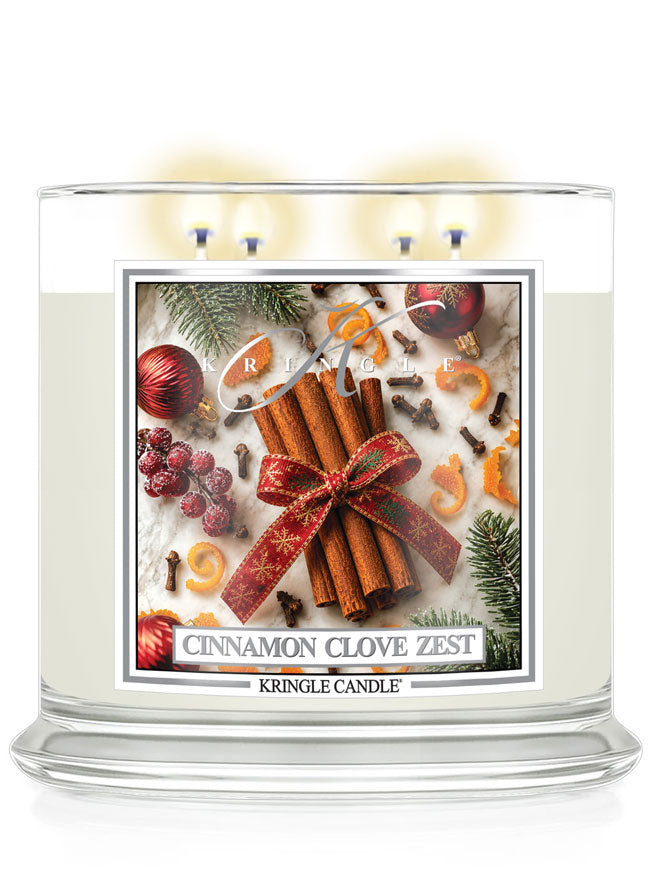 A large glass jar candle labeled 'Cinnamon Clove Zest' by Kringle Candle, with three lit wicks at the top and a festive label showing cinnamon sticks, pine branches, berries, and holiday ornaments on a white background.