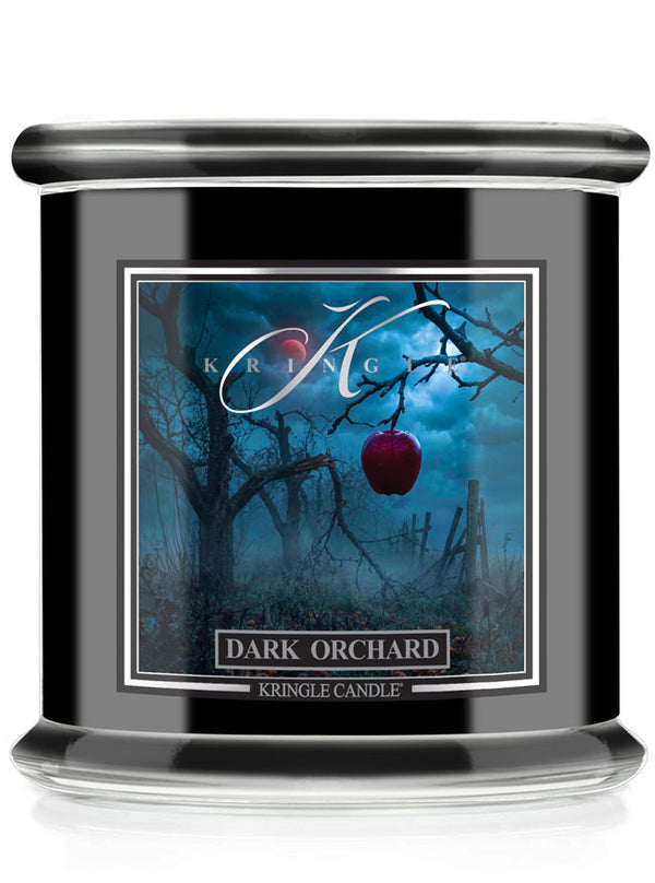 A Halloween-themed Kringle Candle jar candle labeled 'Dark Orchard' with a black body, clear glass base, and a front label showing a dark blue orchard scene with bare trees and a red apple.