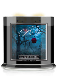 A Halloween Kringle Candle jar labeled 'Dark Orchard' with a black glass container, white wax visible at the top, and a front label showing a spooky blue orchard scene with bare trees and a red apple.
