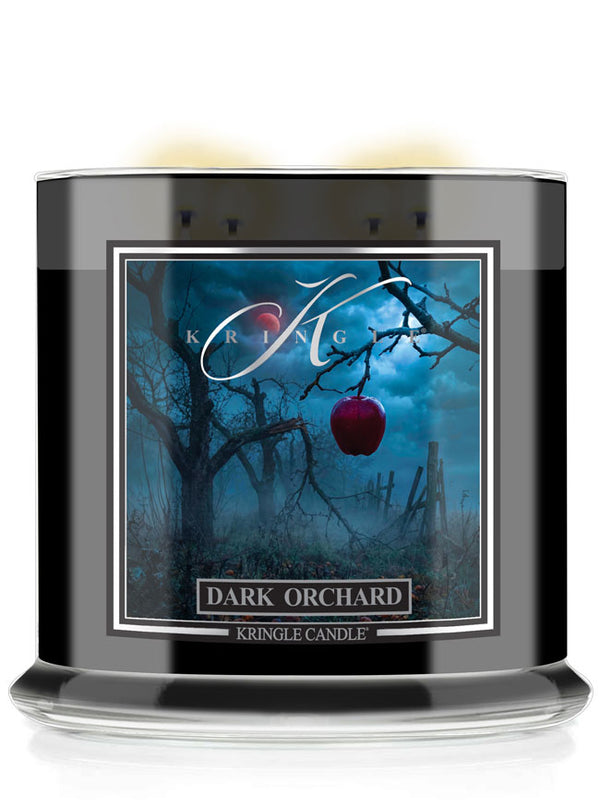 A Halloween Kringle Candle jar labeled 'Dark Orchard' with a black glass container, white wax visible at the top, and a front label showing a spooky blue orchard scene with bare trees and a red apple.
