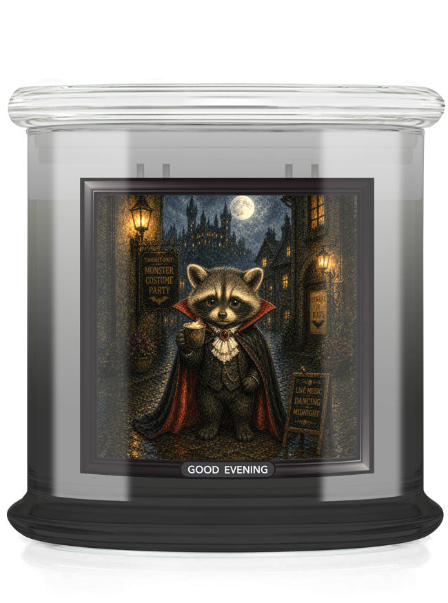 A glass jar candle with a black base and a printed front label showing a raccoon dressed as a vampire in a moonlit street scene. The label reads 'GOOD EVENING'.