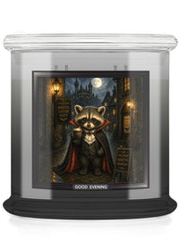 A glass jar candle with a black base and a printed front label showing a raccoon dressed as a vampire in a moonlit street scene. The label reads 'GOOD EVENING'.