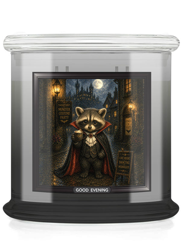 A glass jar candle with a black base and a printed front label showing a raccoon dressed as a vampire in a moonlit street scene. The label reads 'GOOD EVENING'.