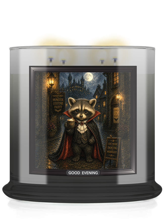 A large glass jar candle with a black base and a printed front label showing a vampire raccoon in a cape on a moonlit street. The candle is lit, with warm yellow wax glowing at the top, and the label reads 'GOOD EVENING'.
