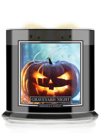 A Kringle Candle jar labeled 'Graveyard Night' with a black container, clear glass base, and a front label showing a glowing jack-o'-lantern against a blue background.