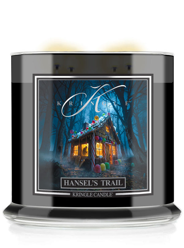 A Kringle Candle jar candle labeled 'Hansel's Trail' with a black glass container, clear base, and a front label showing a haunted house in a dark blue forest at night.