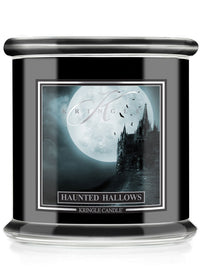 A Kringle Candle jar candle with a black body, featuring a gothic Halloween label that reads 'Haunted Hallows' and shows a haunted house silhouette against a full moon.