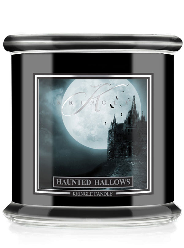 A Kringle Candle jar candle with a black body, featuring a gothic Halloween label that reads 'Haunted Hallows' and shows a haunted house silhouette against a full moon.
