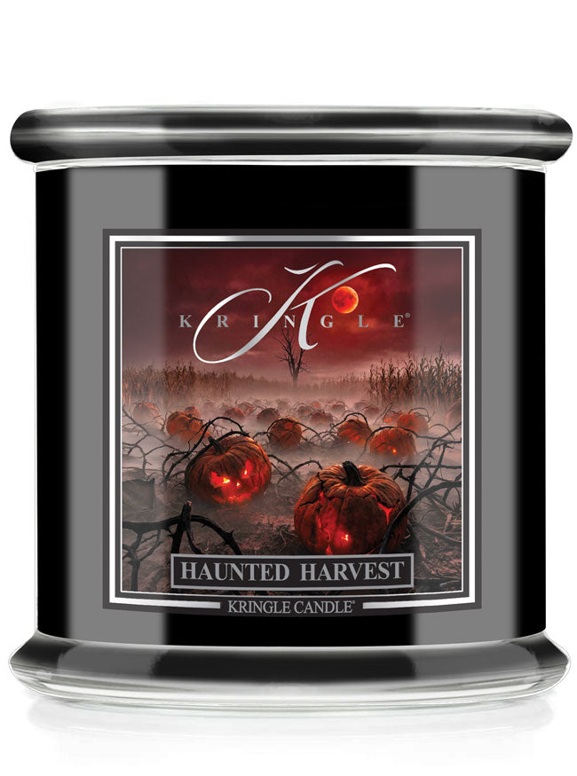 A Kringle Candle in a black glass jar featuring a Halloween-themed label that reads 'Haunted Harvest' with glowing pumpkins and a red full moon.