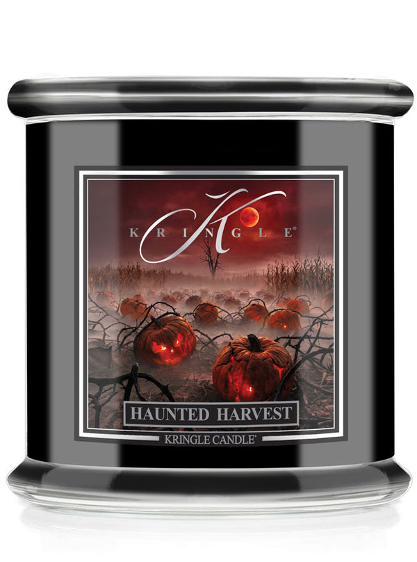 A Kringle Candle in a black glass jar featuring a Halloween-themed label that reads 'Haunted Harvest' with glowing pumpkins and a red full moon.