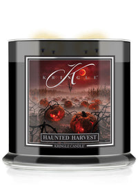 A Kringle Candle jar labeled 'Haunted Harvest' with a black container, clear glass base, and a front label showing glowing pumpkins, bare branches, and a red sky.