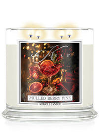 A Kringle Candle in a clear glass jar with three lit wicks, featuring a festive label for 'Mulled Berry Pine' with an illustration of a berry drink, orange slices, and holiday lights.