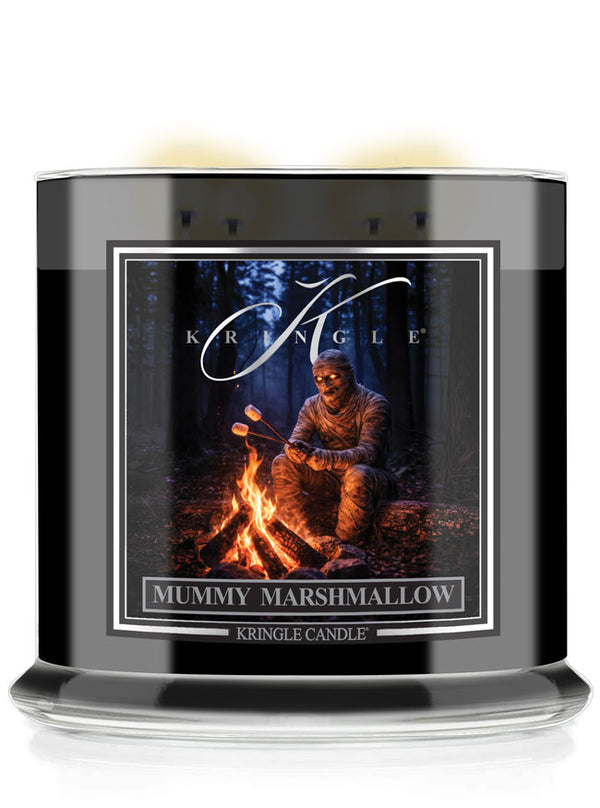 A Kringle Candle jar labeled 'Mummy Marshmallow' with a black container, clear glass base, and a front label showing a person sitting by a campfire in a dark forest.