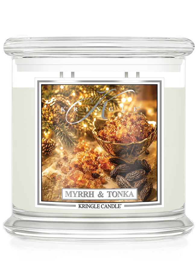 A Kringle Candle jar candle labeled 'Myrrh & Tonka' with a clear glass container, white wax, and a decorative front label showing amber resin, spices, and warm holiday lighting.