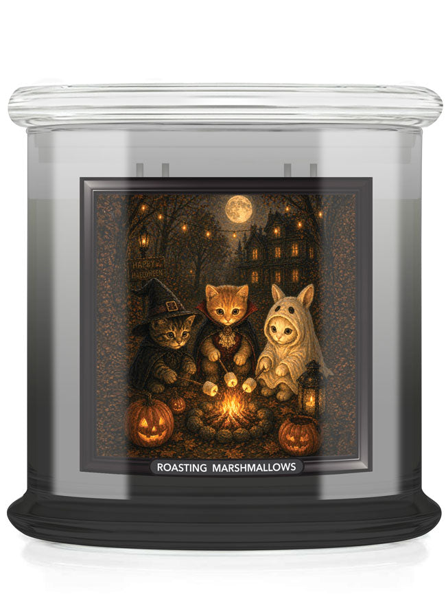 A large scented candle in a clear glass jar with a black base, featuring a Halloween-themed illustration on the front label. The artwork shows three cats dressed as a witch, a cat, and a rabbit, gathered around a warm fire with pumpkins, a haunted house and roasting marshmallows under a full moon.