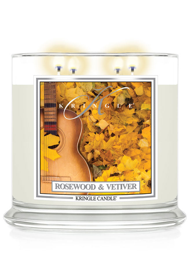 Lit 4-wick candle in a clear jar with a label of an acoustic guitar amidst yellow autumn leaves.