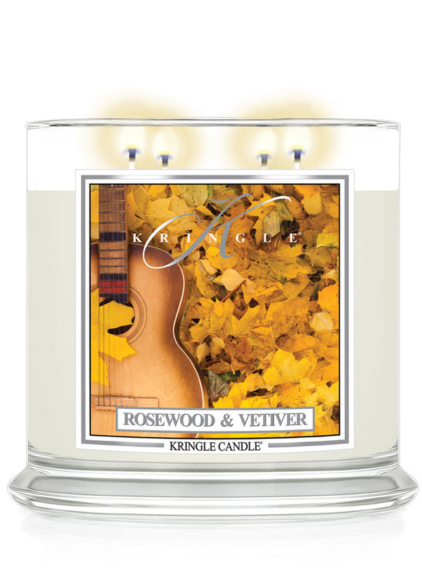 Lit 4-wick candle in a clear jar with a label of an acoustic guitar amidst yellow autumn leaves.