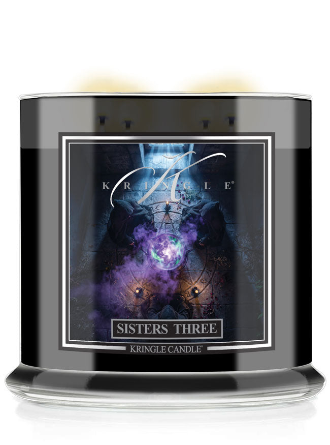 A black glass jar candle with a detailed front label reading 'Kringle Candle Sisters Three'. The Halloween label features a dark, mystical graphic with purple and blue tones.