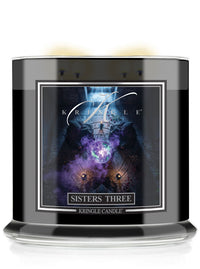 A black glass jar candle with a detailed front label reading 'Kringle Candle Sisters Three'. The Halloween label features a dark, mystical graphic with purple and blue tones.