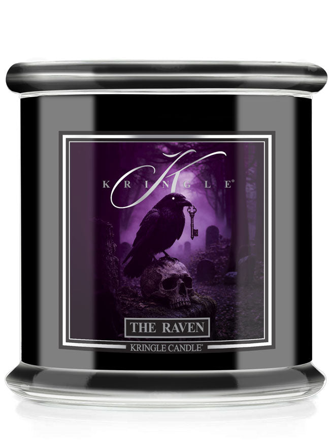 A Kringle Candle jar candle with a black body and lid, featuring a Halloween gothic label with a raven perched on a skull in a purple misty forest scene. The label reads 'KRINGLE CANDLE' and 'THE RAVEN'.