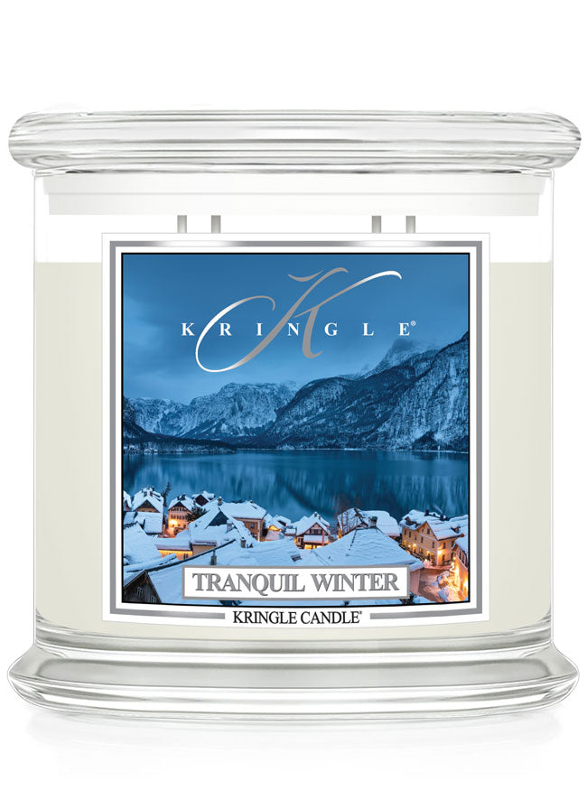 A Kringle Candle in a clear glass jar with white wax, featuring a square label that reads 'Tranquil Winter' and shows a snowy mountain village by a lake.