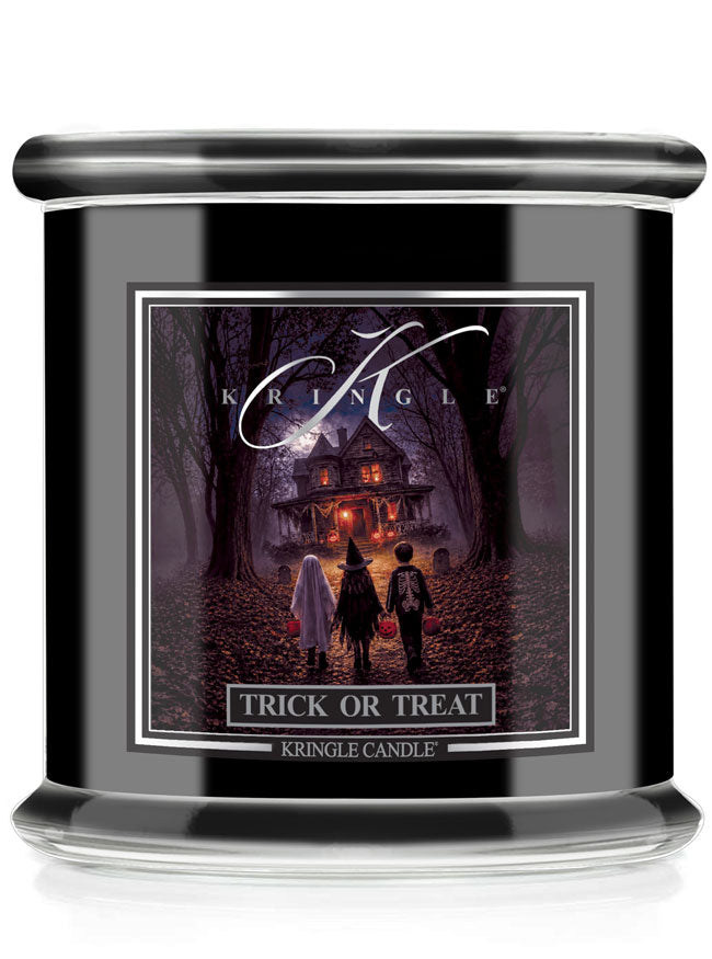 A black glass jar candle with front label reading 'KRINGLE' and 'TRICK OR TREAT'. The label features a spooky illustration of three children standing in a dark forest path toward a haunted house.