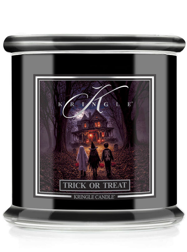 A black glass jar candle with front label reading 'KRINGLE' and 'TRICK OR TREAT'. The label features a spooky illustration of three children standing in a dark forest path toward a haunted house.