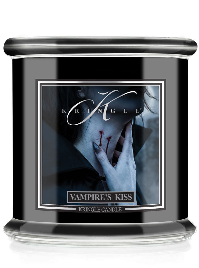 A Halloween Kringle Candle jar candle labeled 'Vampire's Kiss' with a black body, clear glass base, and a front label showing a moody portrait of a hand near a neck with red bite marks.