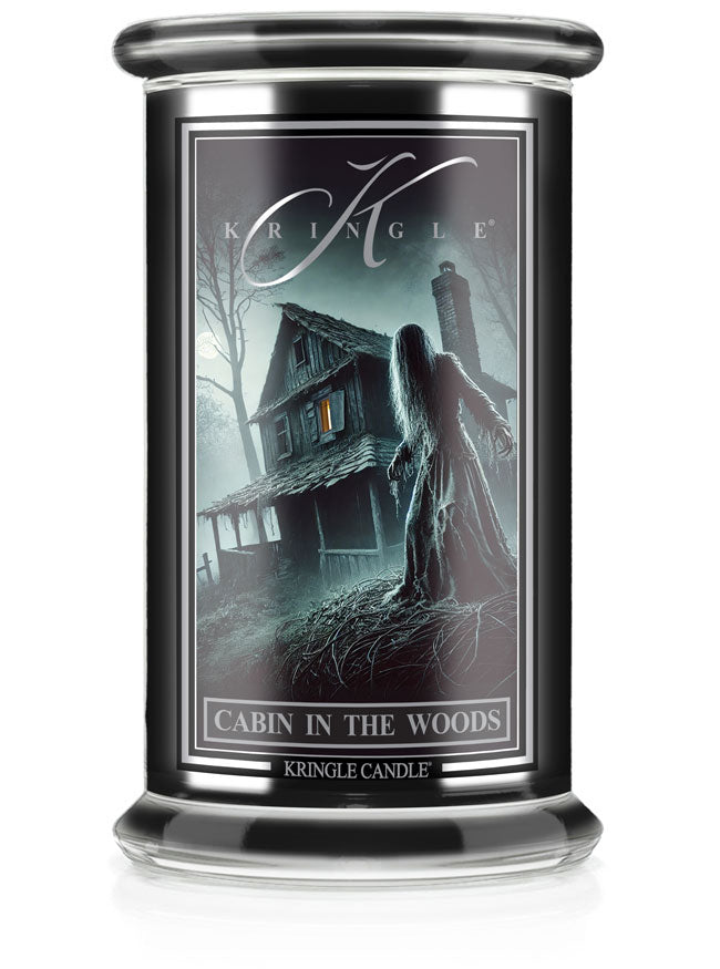 Unlit Halloween candle labeled "Cabin in the Woods" with eerie cabin and figure in a dark forest scene.