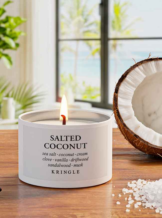 Kringle Candle salted coconut candle on a wooden surface with a window and plant in the background